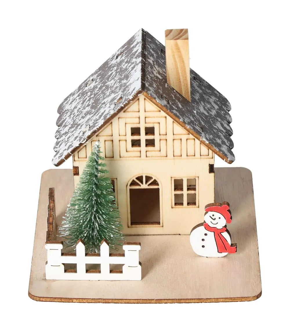 Wooden house with snow-topped roof, snowman, Christmas tree, and fence on a wooden base, representing a festive decoration theme.
