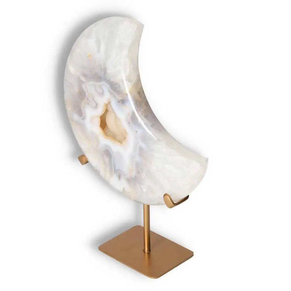 Ethereal agate lunar crescent sculpture with natural geode, showcasing swirling off-white hues, displayed on a sleek gold stand.