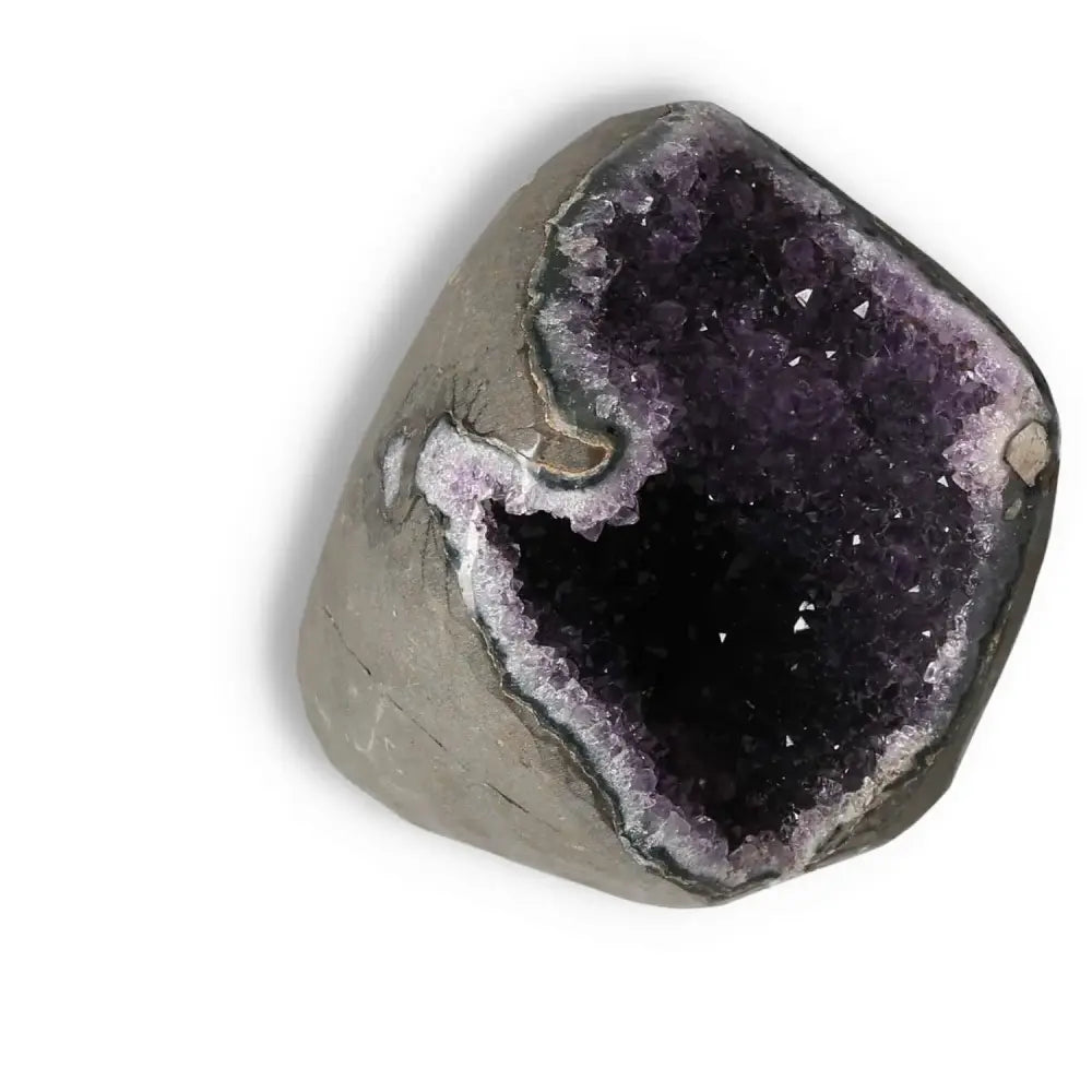 Amethyst Cut Base Geode from Sylvia Crystals surrounded by rough stone, showcasing sparkling purple crystals ideal for stress reduction and energy boost.