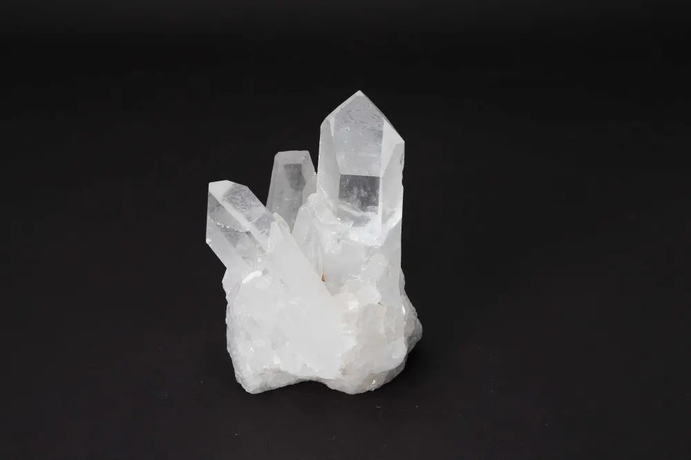 Clear quartz cluster on black background, showcasing its natural crystal points and light-amplifying properties.