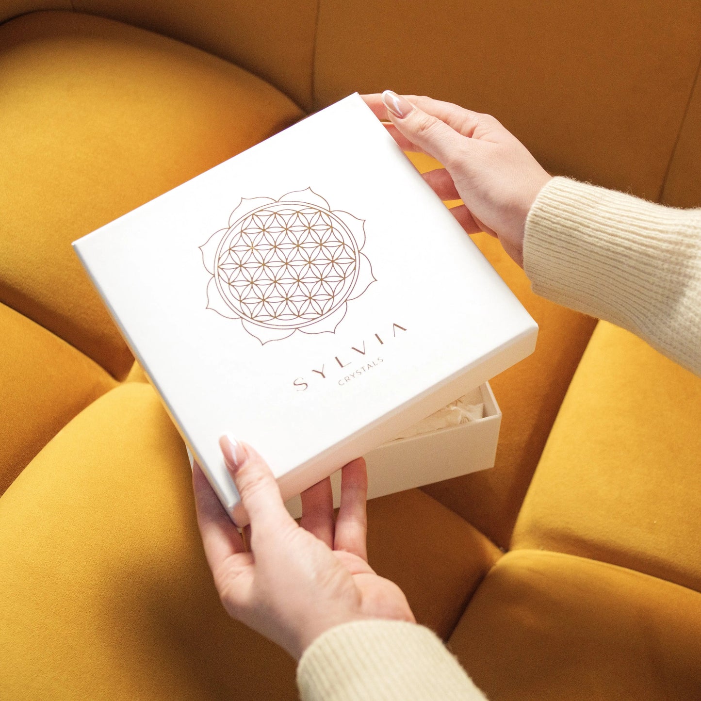 Hands opening Eternal Love Gift Box with Carnelian Hearts on yellow sofa, a perfect Valentine's Day present symbolizing love and courage.
