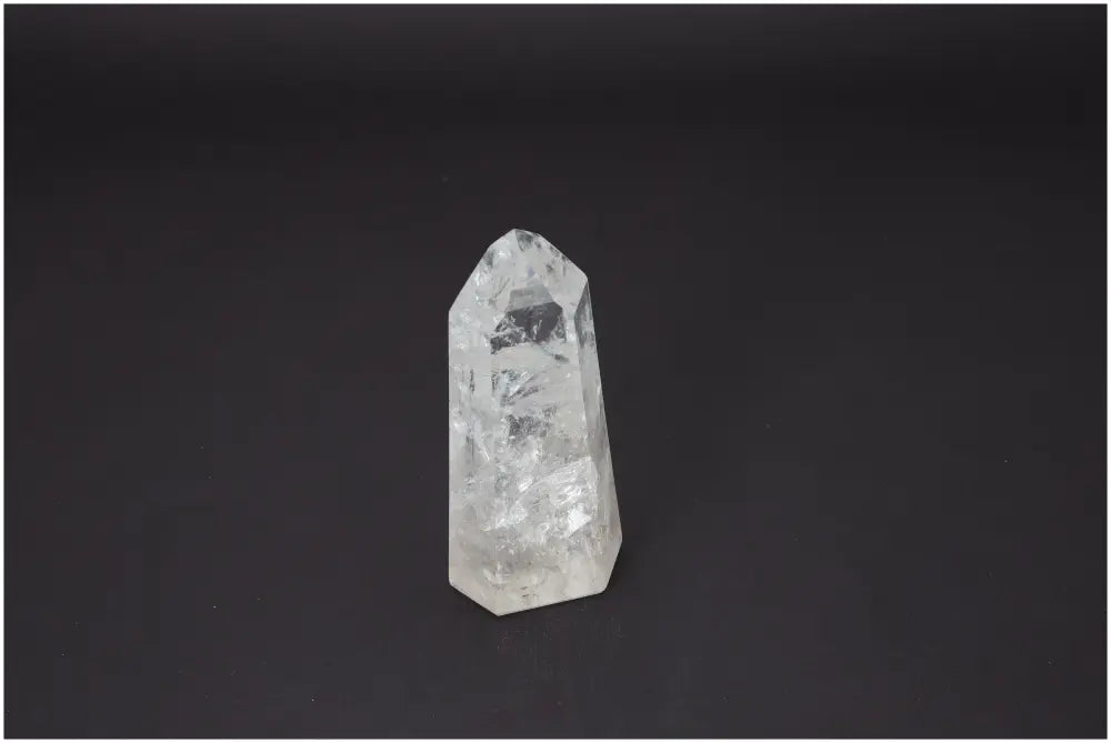 Clear Lemurian Quartz Obelisk against a dark background, known for its unique energetic properties and associations with chakras and zodiac signs.