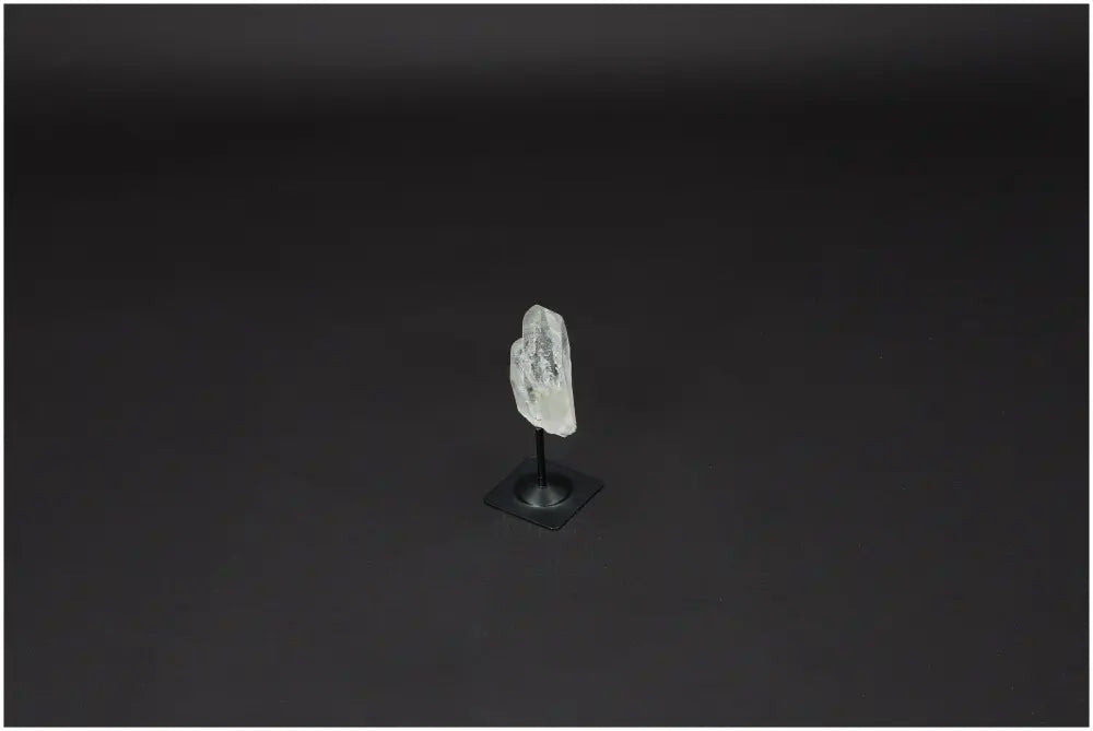 Lemurian Quartz crystal on sleek metal stand, known for clarity and healing, against a dark backdrop.