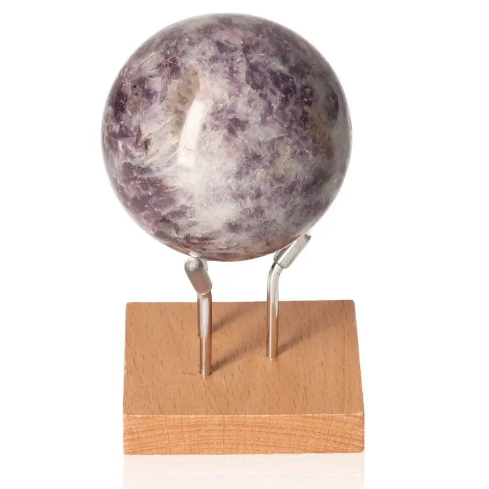 Lepidolite sphere with soothing purple hues, promoting emotional balance and peace, on a wooden stand for decorative display.