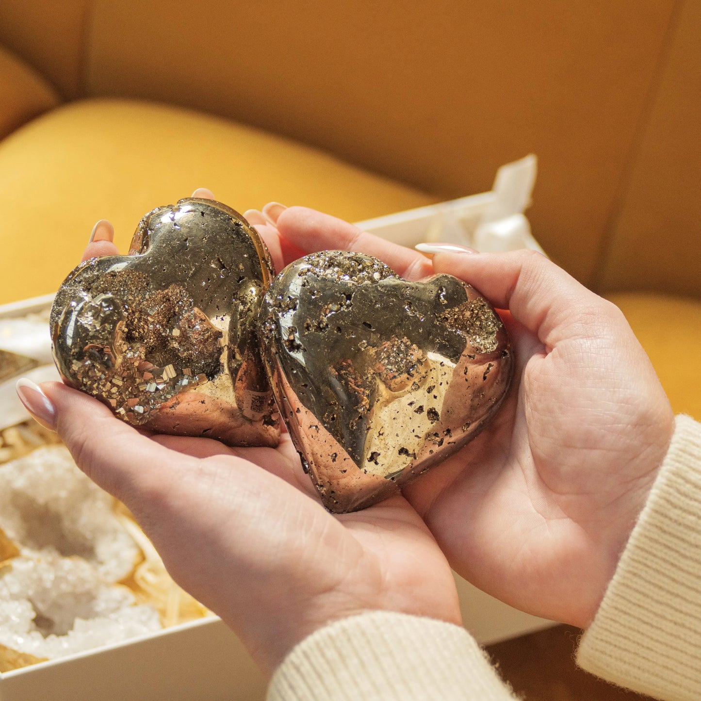 Hands holding two polished pyrite hearts from Sylvia Crystals' Love and Wealth Gift Box, symbolizing love and prosperity.