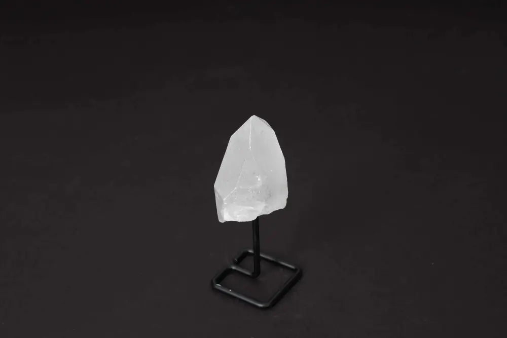 Natural Clear Quartz Point on black metal stand against dark background, showcasing its clarity and elegant finish.