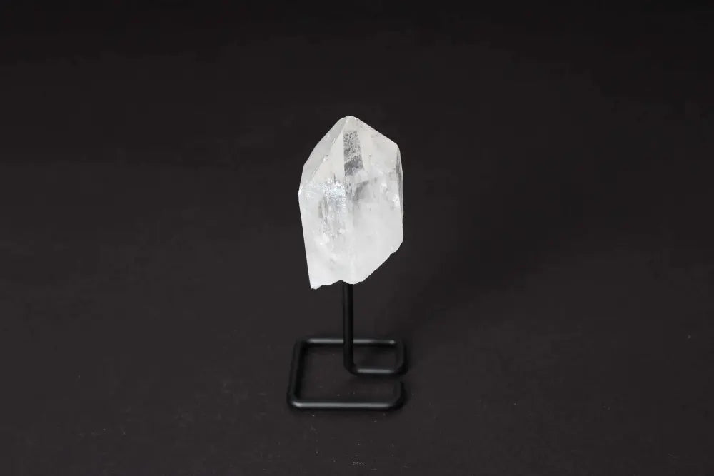 Clear quartz crystal point on a sleek black stand, known for energy amplification and clarity, ideal for meditation and energy work.