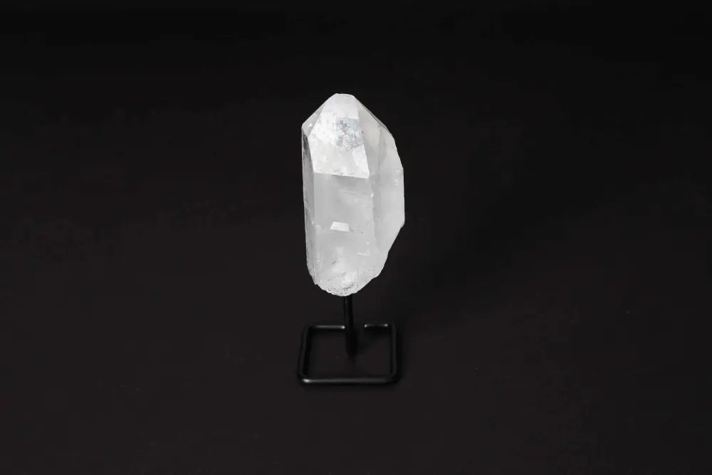 Natural clear quartz point on a black stand against a dark background, known for energy amplification and clarity enhancement.