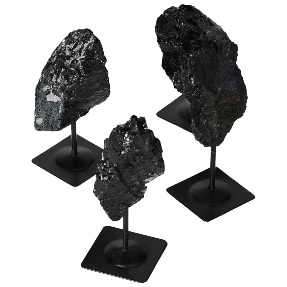 Rough tourmaline gemstones on metal stands, showcasing deep blacks and vibrant greens, symbolizing luxury and spiritual harmony.
