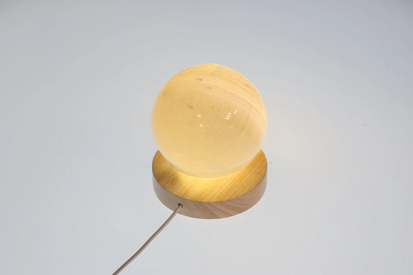 Selenite sphere 6cm on stand, glowing softly, ideal for mindful living and spiritual growth by Sylvia Crystals.