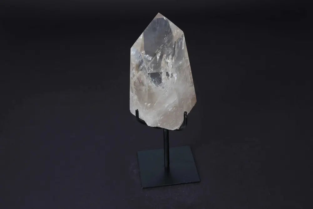 Semi polished clear quartz point on stand, ideal for amplifying energy and meditation, elegantly displayed on a black base.