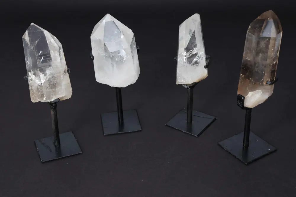 Four clear quartz points on stands for energy amplification and meditation, displayed on a dark background.