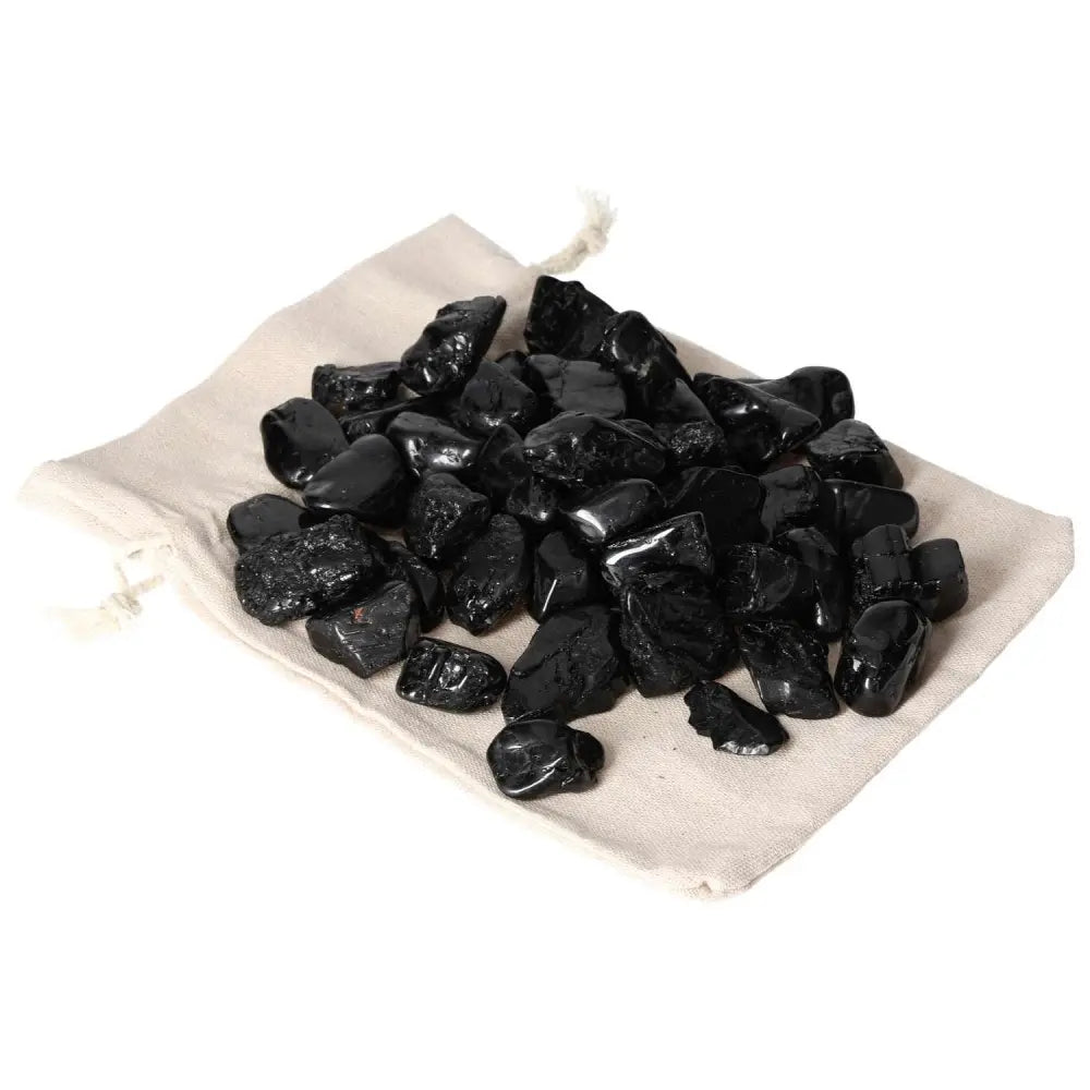 Tumbled Black Tourmaline M stones from Sylvia Crystals on a beige pouch, known for shielding against negativity and enhancing clarity.