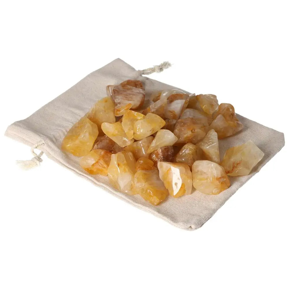 Assorted tumbled yellow hematoid crystals on a beige cloth showcasing their golden hues, representing luxury and elegance.