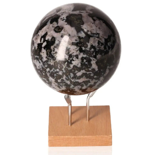 Indigo Gabbro sphere on wooden stand, known as Mystic Merlinite, enhances intuition and spiritual growth with black and indigo patterns.