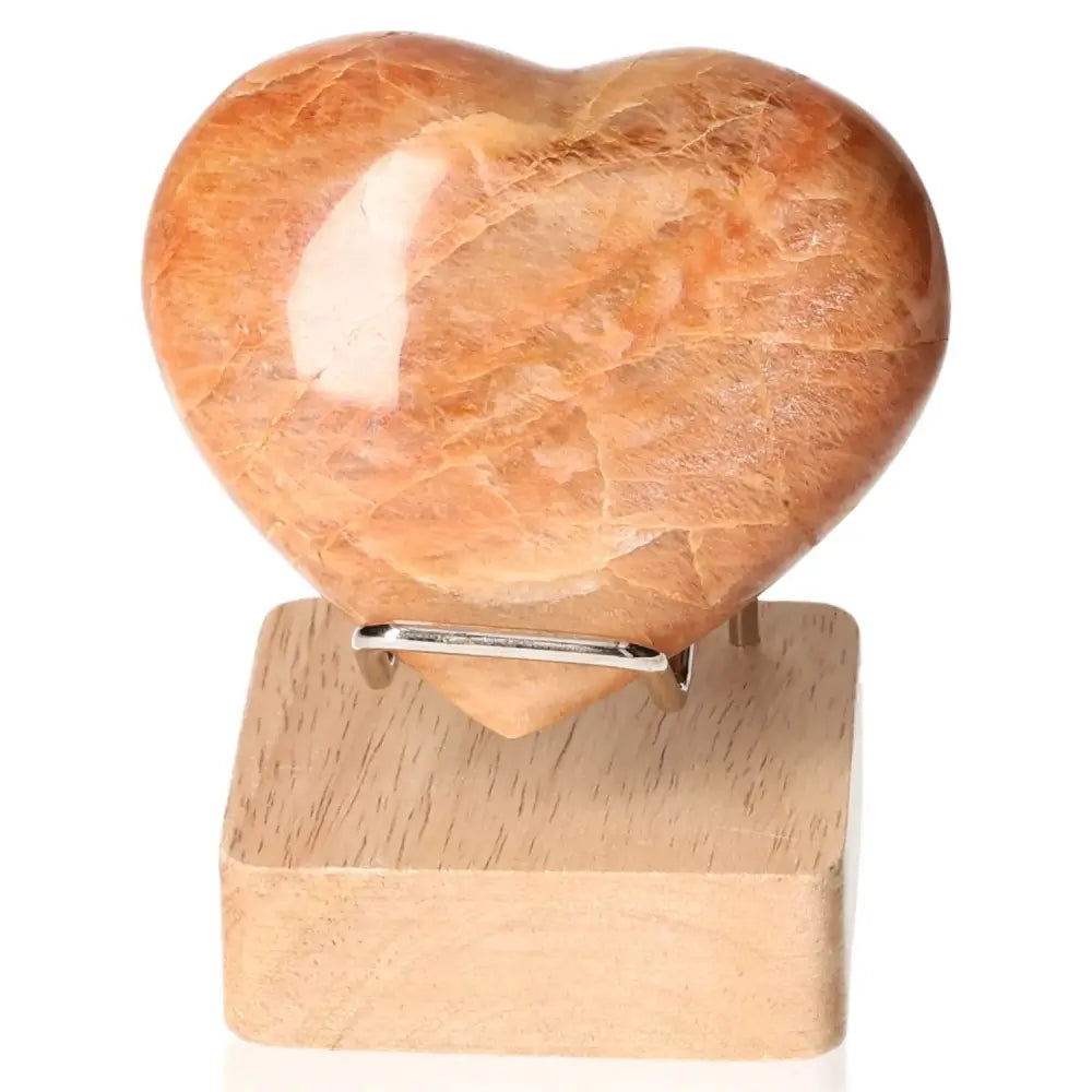 Peach Moonstone Heart crystal for emotional balance, enhancing intuition and protection against nightmares, displayed on a wooden stand.