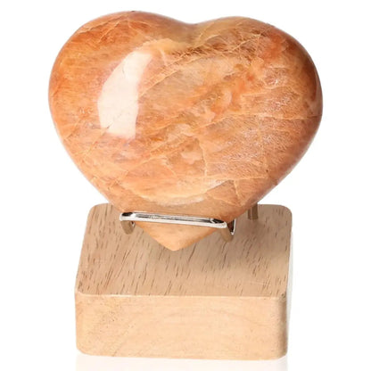 Peach Moonstone Heart crystal for emotional balance, enhancing intuition and protection against nightmares, displayed on a wooden stand.
