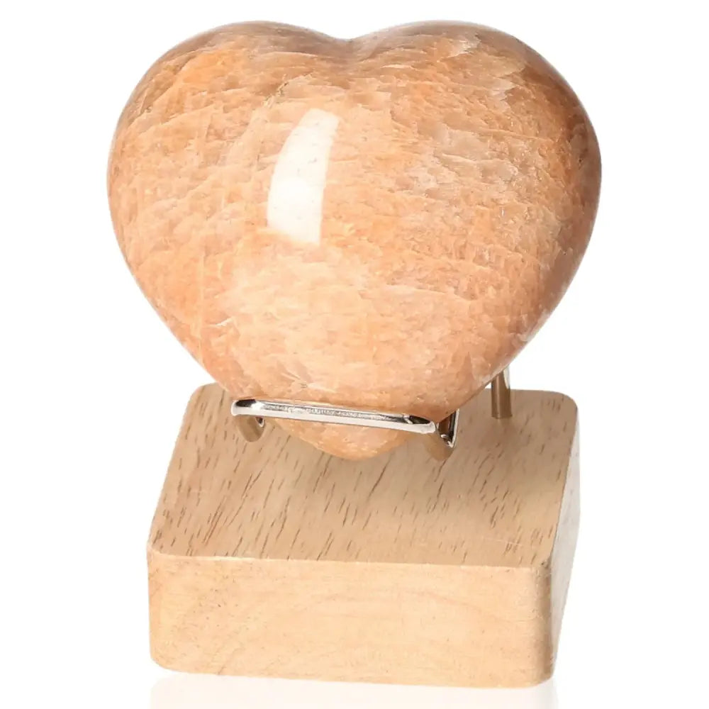 Peach Moonstone Heart promoting emotional balance and intuition on a wooden stand, enhancing sleep and attractiveness.