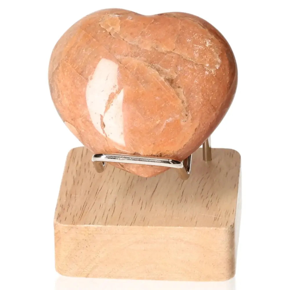 Peach Moonstone Heart Crystal promoting emotional balance and intuition displayed on a wooden stand, perfect for enhancing well-being.