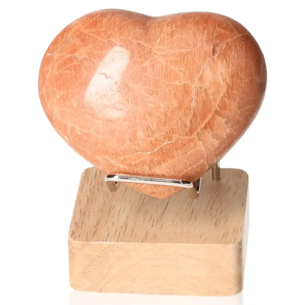 Peach Moonstone Heart promoting emotional balance and intuition, displayed on a wooden stand. Stand not included.