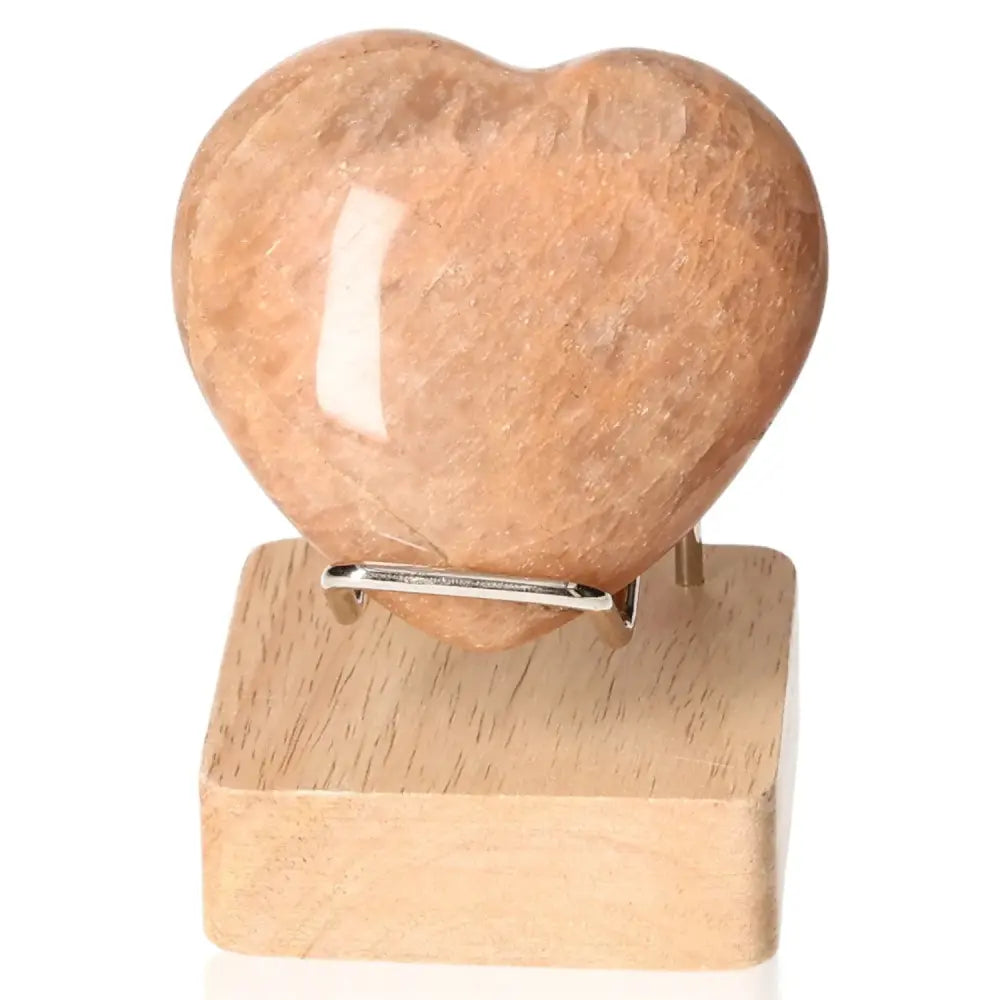 Peach moonstone heart gemstone on wooden stand, enhances emotional balance and intuition, ideal for restful sleep and protection.