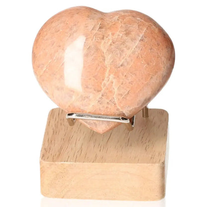 Peach Moonstone heart-shaped crystal for emotional balance and intuition, shown on a wooden stand. Stand not included.