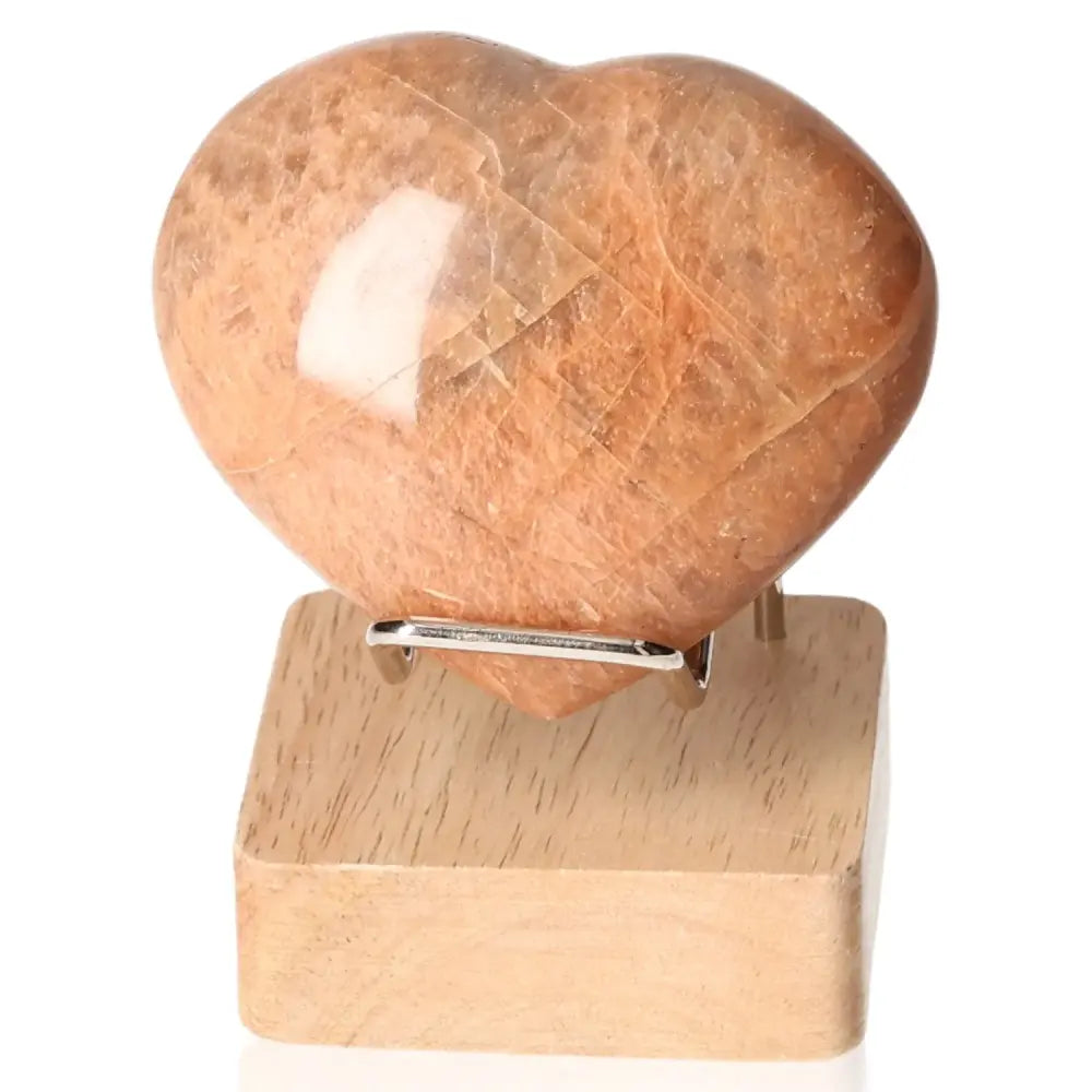 Peach Moonstone Heart promoting emotional balance and intuition, placed on a wooden stand, perfect for enhancing sensitivity and restful sleep.