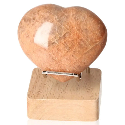 Peach Moonstone Heart promoting emotional balance and intuition, placed on a wooden stand, perfect for enhancing sensitivity and restful sleep.