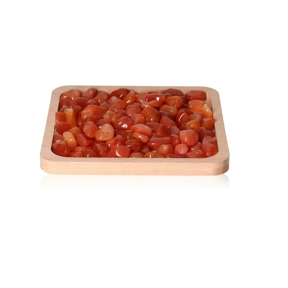 Vibrant orange-red Carnelian gems in a wooden tray, symbolizing motivation and vitality, curated by Sylvia Crystals for luxury elegance.