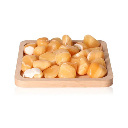 Tumbled Orange Calcite stones on a wooden tray, promoting self-confidence and learning with positive energy.