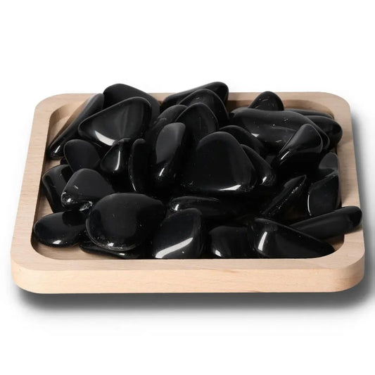 Tumbled Obsidian stones on a wooden tray, known for protective energy and absorbing negativity, creating a serene environment.