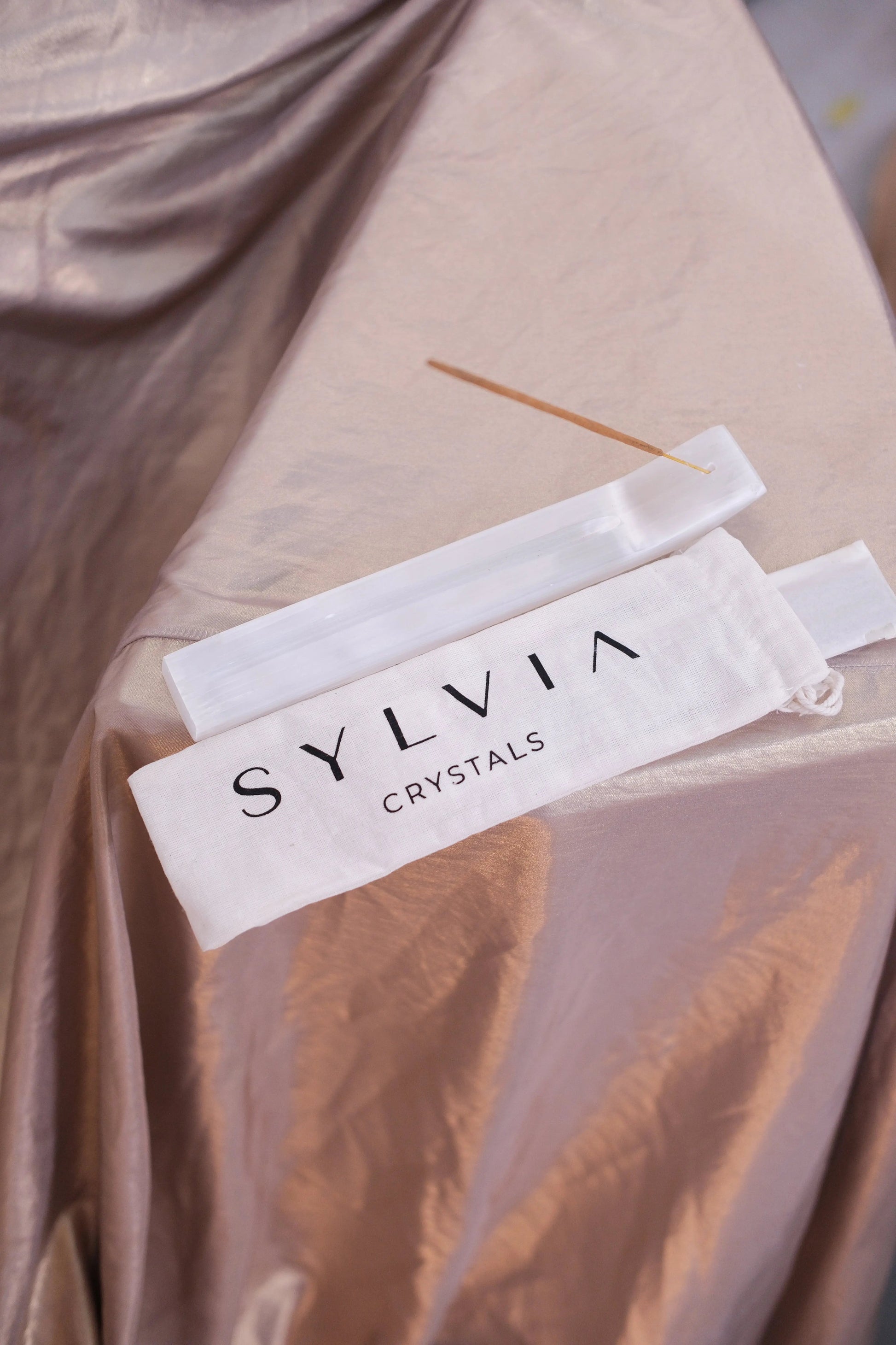 Incense stick resting on a satin cloth with branded Sylvia Crystals packaging.