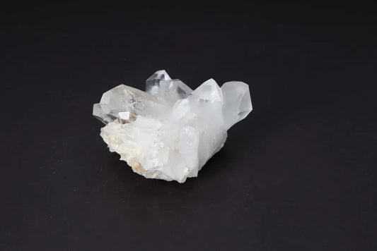 Clear quartz cluster with multiple crystal points on a dark background, radiating light and high vibrational energy.