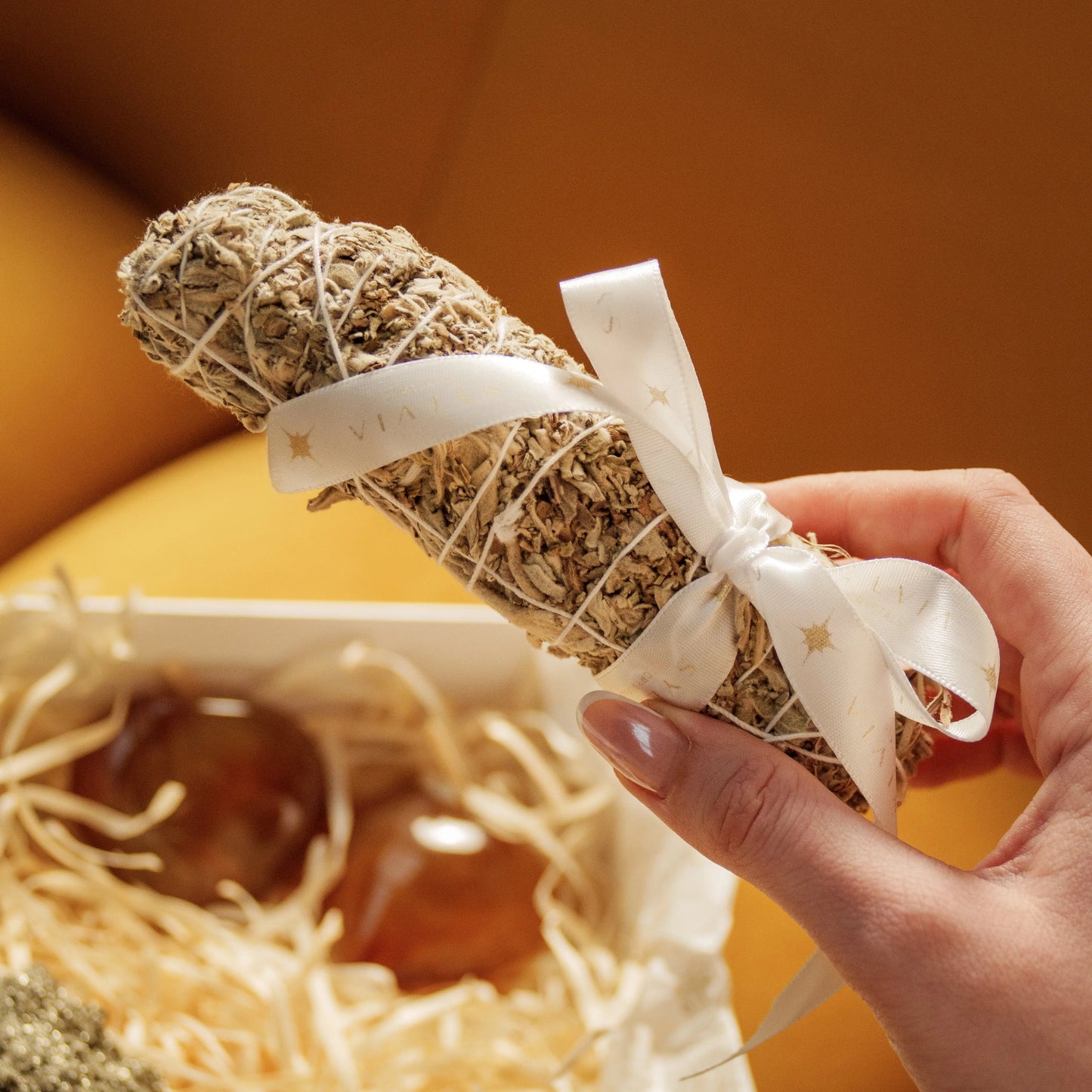 Hand holding white sage bundle above Eternal Love Gift Box with Carnelian Hearts and Rough Pyrite for Valentine's Day