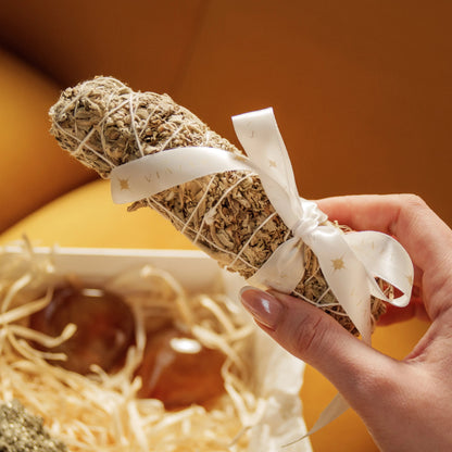 Hand holding white sage bundle above Eternal Love Gift Box with Carnelian Hearts and Rough Pyrite for Valentine's Day