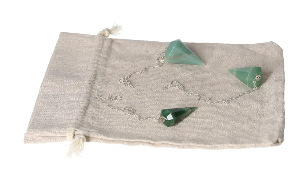 Green quartz pendulum with silver chain on beige drawstring pouch for dowsing and spiritual practice.