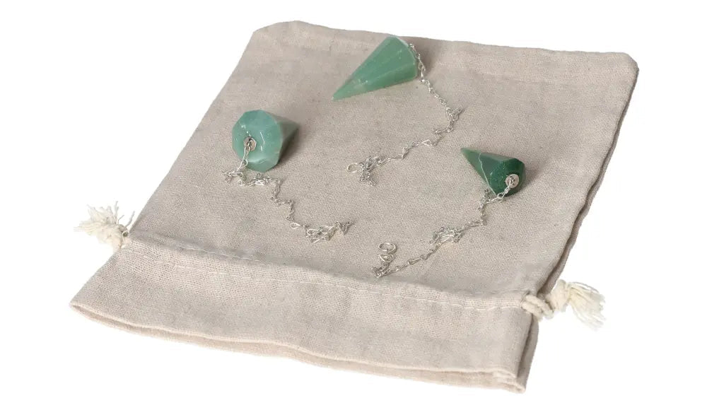 Green quartz pendulum laid on a beige fabric pouch, featuring silver chains and pointed crystal tips for dowsing and divination.