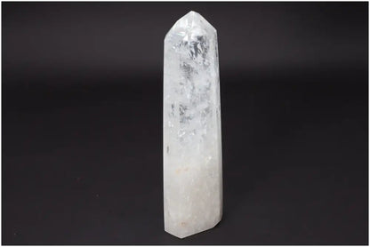 Lemurian Quartz Obelisk crystal, clear and elongated, standing upright against a dark background, symbolizing clarity and balance.