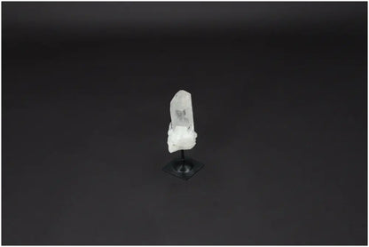 Clear Lemurian Quartz crystal on black metal stand against dark background, embodying clarity and balance.