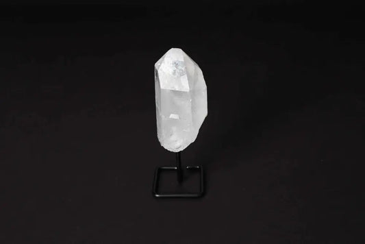 Natural clear quartz point on a black stand against a dark background, known for energy amplification and clarity enhancement.