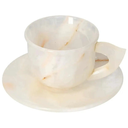 Off-white onyx coffee cup and plate set, showcasing unique patterns and a polished surface that reflects soft light, enhancing elegance.