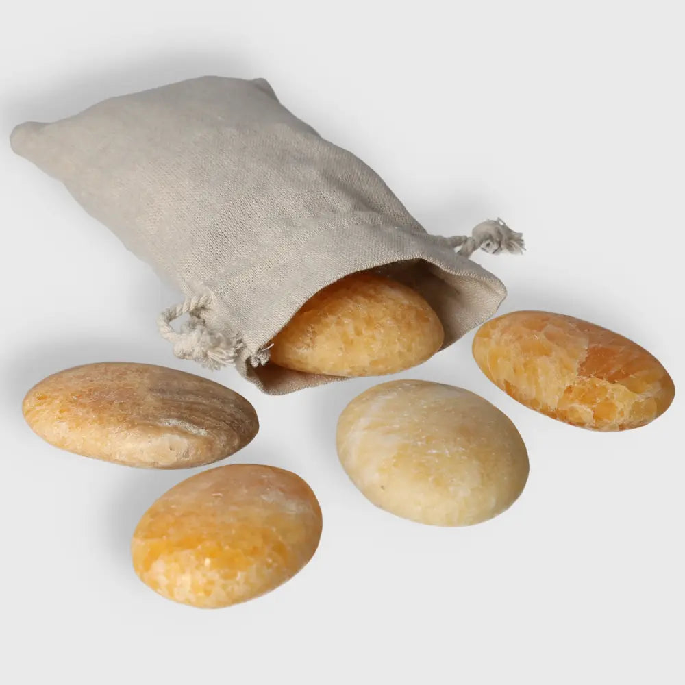Five smooth orange calcite palm stones spilling from a canvas pouch, perfect for meditation and emotional healing.