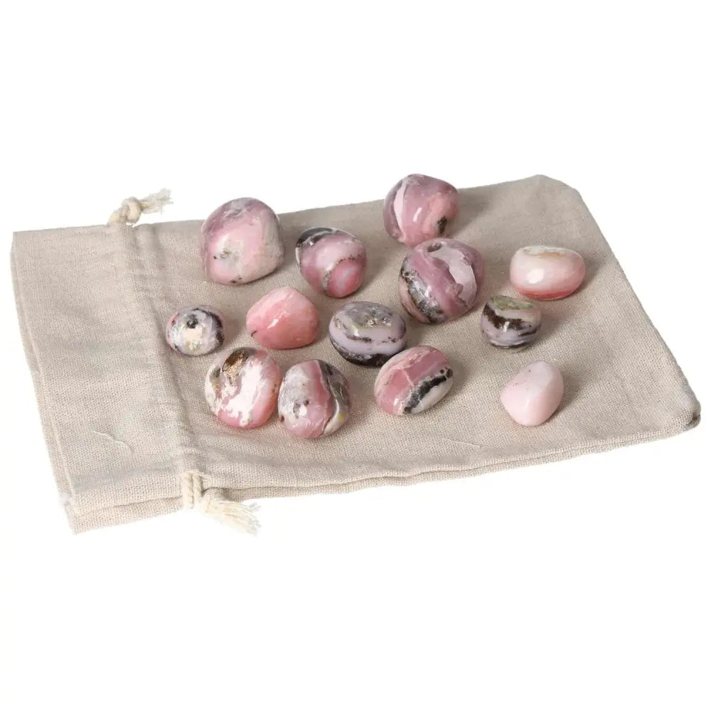 Pink Opal tumbled stones displayed on a cloth bag, showcasing soft pastel pink hues and smooth, soothing appearance.