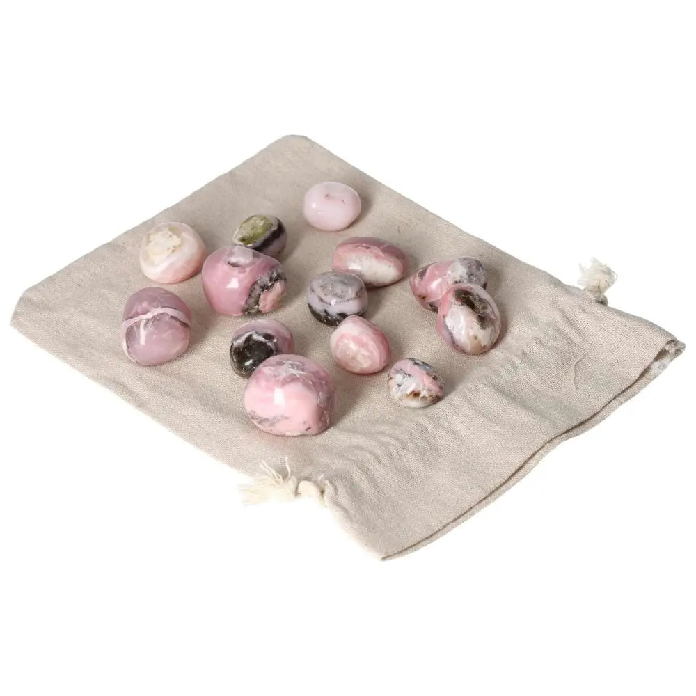Assorted pink opal tumbled stones on a beige cloth, showcasing gentle pastel hues and smooth surfaces for emotional healing and renewal.