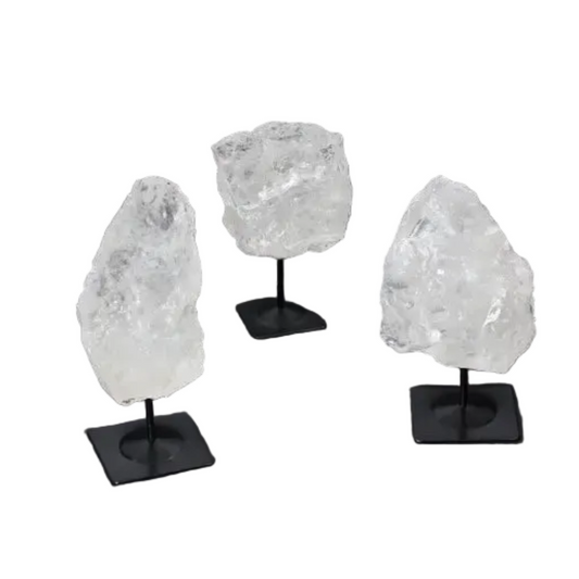 Three rough clear quartz crystals on metal stands, used for purification and harmonizing, displayed on a dark background.
