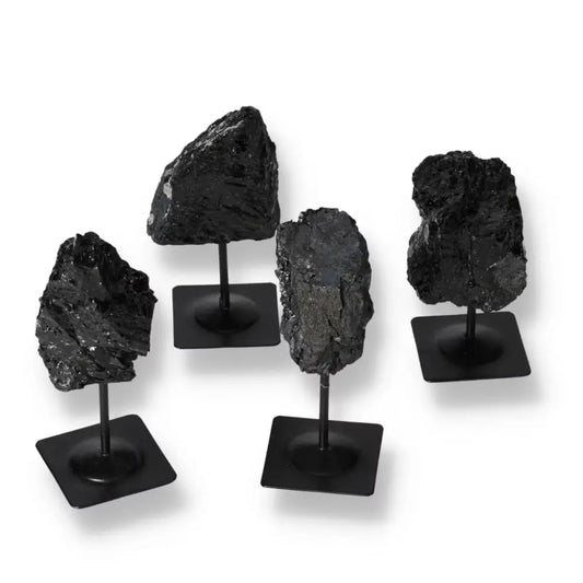 Rough Tourmaline stones on metal stands showcasing deep blacks and greens, from Sylvia Crystals, symbolizing luxury and spiritual harmony.