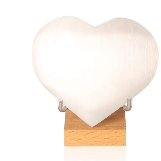 10cm Selenite heart crystal by Sylvia Crystals on a wooden stand, promoting purity and spiritual growth with mindful living.