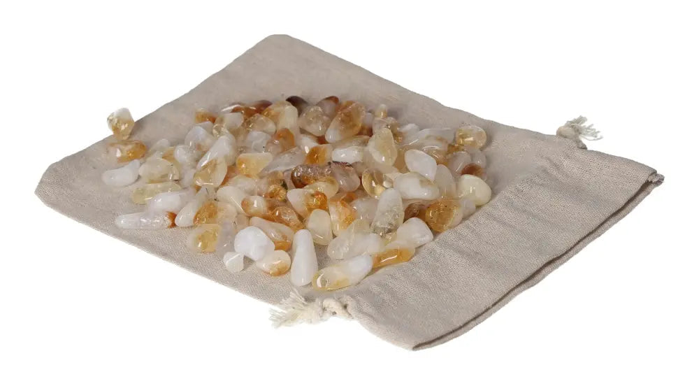 Pile of tumbled citrine and quartz stones on a beige drawstring pouch, symbolizing inspiration and abundance.
