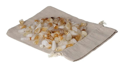 Pile of tumbled citrine and quartz stones on a beige drawstring pouch, symbolizing inspiration and abundance.