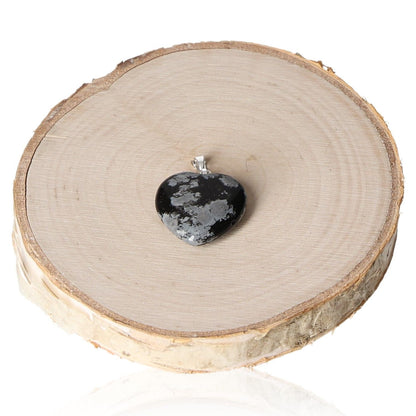 Obsidian snowflake heart pendant 20mm on wooden slice, showing unique natural pattern and craftsmanship.